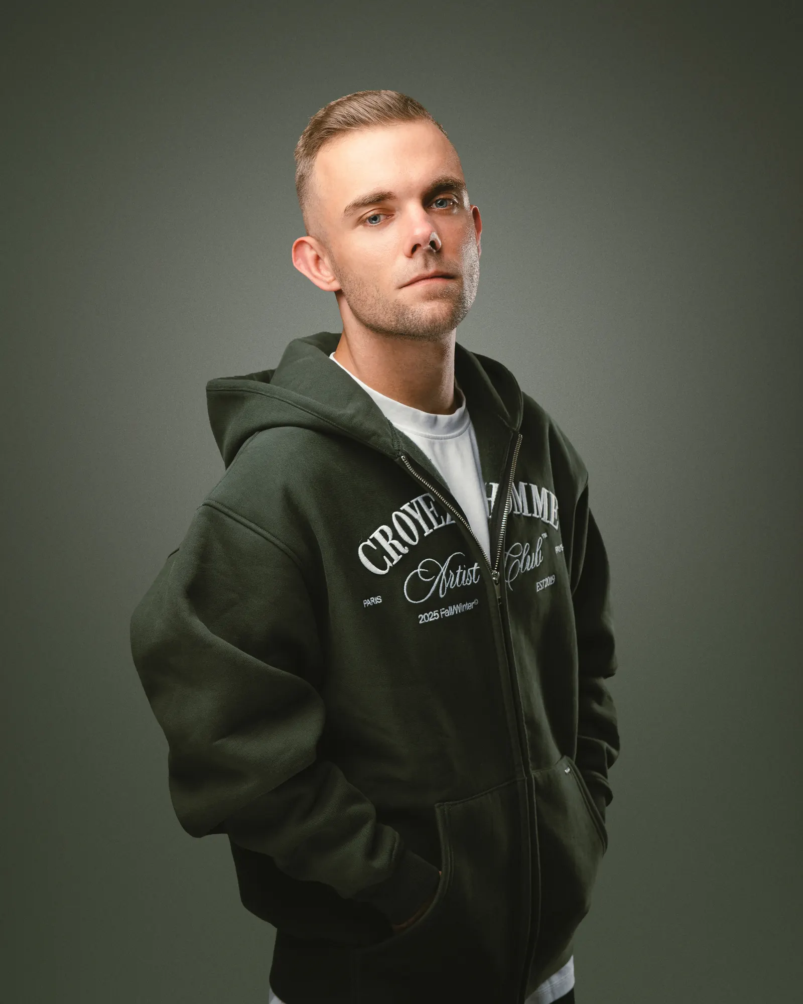 SDNX in donkergroene hoodie, studioportret uit zijn perskit 2026